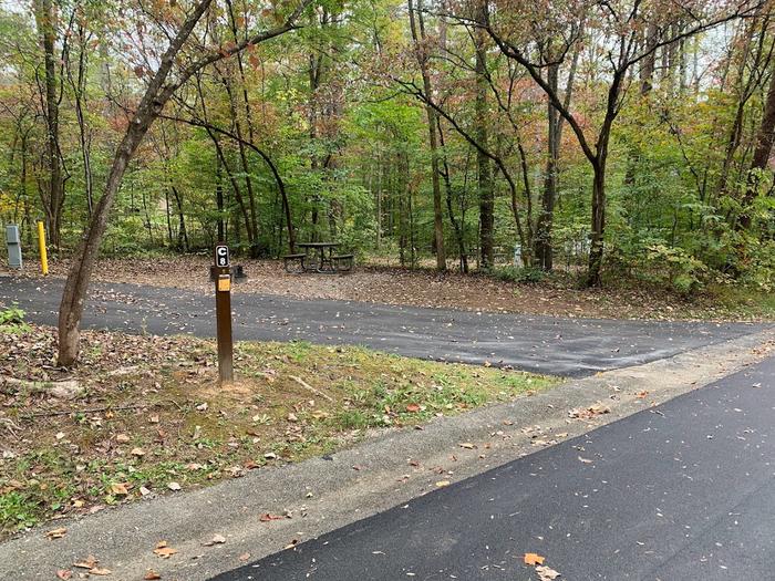 A blacktop surface with green grass on the sides with a small brown post.