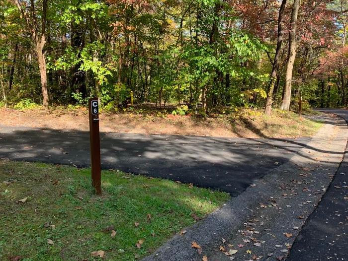 A blacktop surface with green grass on the sides with a small brown post.