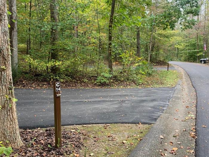 A blacktop surface with green grass on the sides with a small brown post.