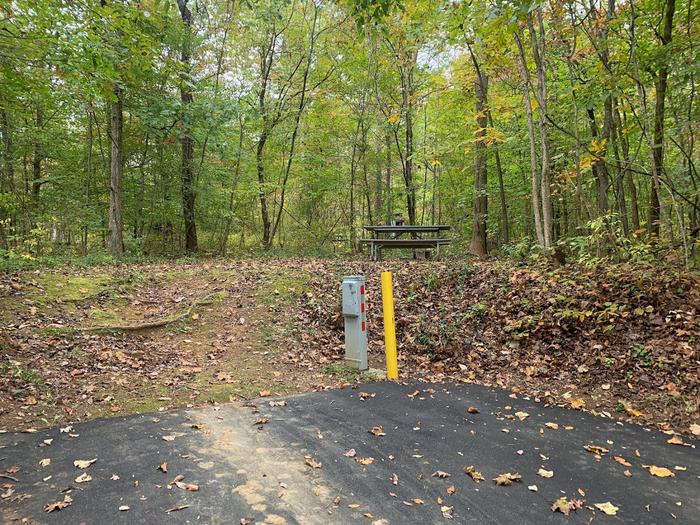 A blacktop surface with a yellow post and gray box near a circle fire ring and picnic table.C-18 has a fire ring and picnic table.
