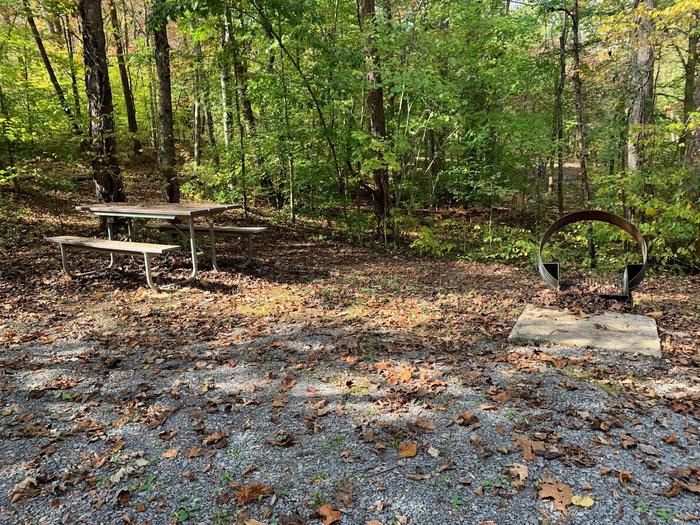 Gravel area with a circle fire pit and picnic table.E-21 tent space.