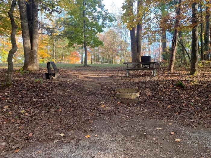 Gravel area with a slight incline with a rock that leads to a circle fire ring and picnic table.F-13 tent space.