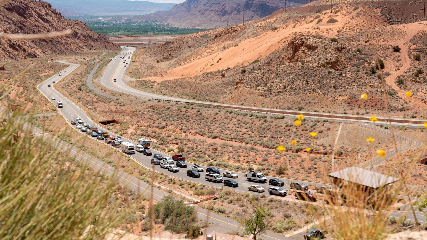 Looking down on the two-lane entrance road to Arches with a line of cars waiting to enter the parkCars in line on the Arches entrance road