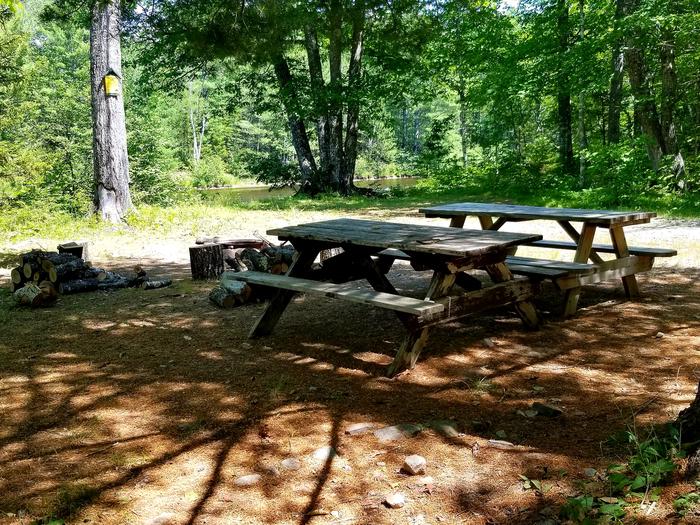 Wooden picnic tables near metal fire ring at Upper East Branch Campsite.A walk-to campsite along the East Branch Penobscot River, Upper East Branch Campsite is located a short distance from the north entrance.