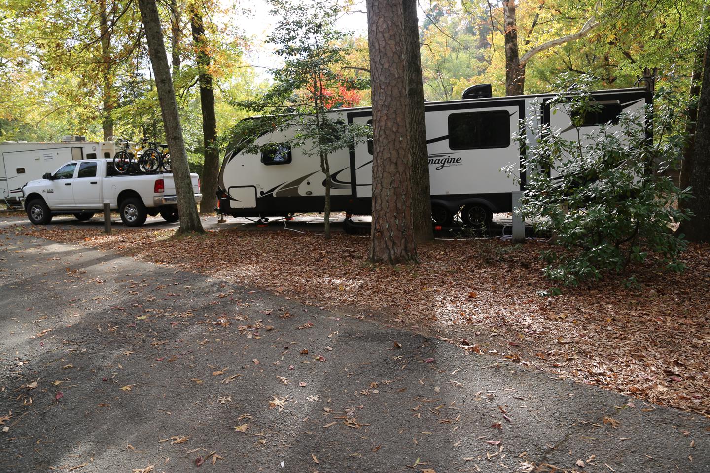 Large RV with full size truck backed in to campsite surrounded by trees and leaves on the ground.Campsite 13