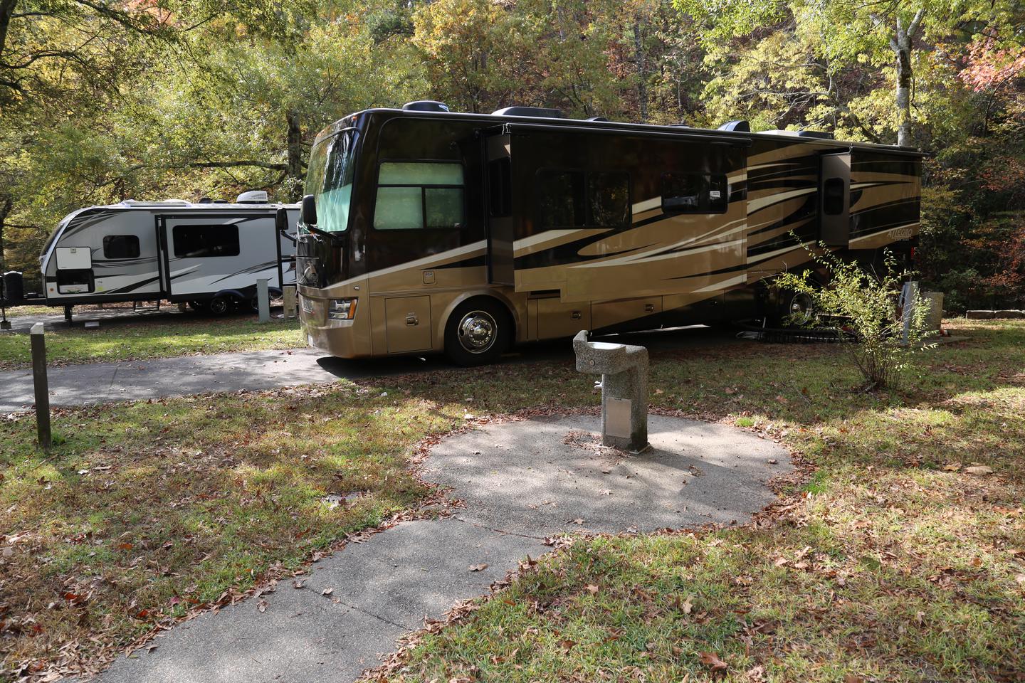 Large RV in paved campsite with trees behind and surrounded by grassCampsite 42