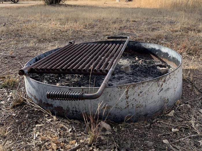 Metal fire pit on the ground at Calabasa campground. Metal ring with an attached metal grill on top.Ground and standing fire pits and grills are available throughout the campground.
