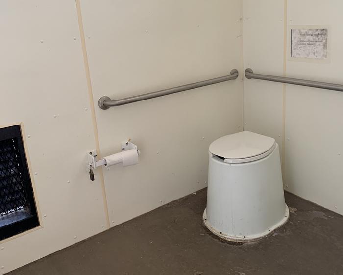 A toilet in the pit toilet building with rolls of toilet paper on the left.Inside the pit toilet building.