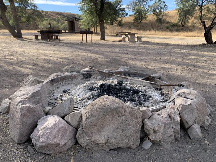 A stone-ringed fire pit on the ground with dark ashes in the center.Stone-ringed fire pit in the central area of the campground.