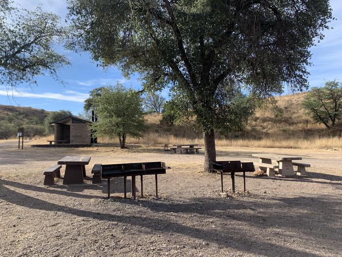 Campground with tables, grills and a pit toilet. Sparse trees and a dry, grassy ecosystemCentral area of the Calabasas Campground.