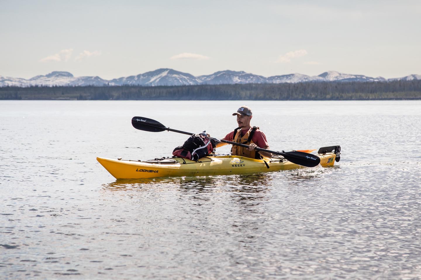Sea kayaker in a yellow boat on a lake with mountains in the backgroundSea kayak on Yellowstone Lake