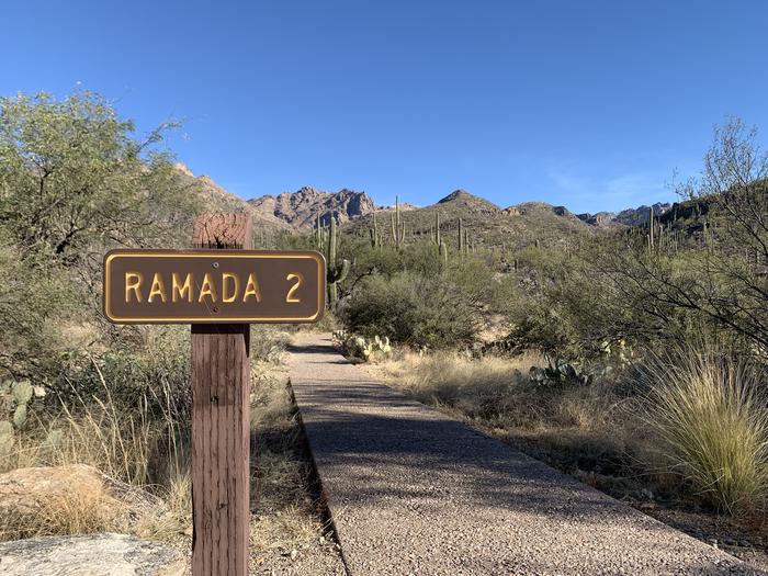 Brown sign to the left of a paved path that says "Ramada 2"Entrance to Ramada 2 from gravel road.