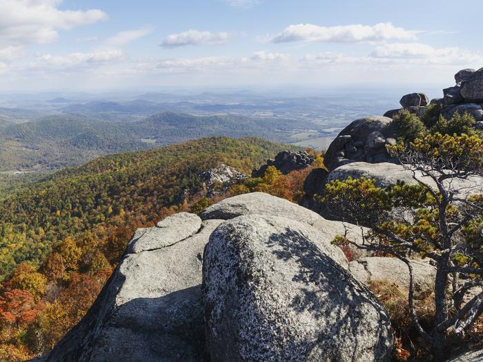 A rock cliff in the foreground of a view overlooking fall colors and rolling mountains. The summit of Old Rag Mountain.