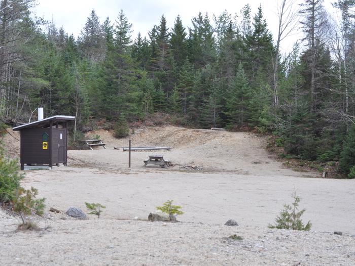 Campsite and brown pit toilet in an open gravelly area.