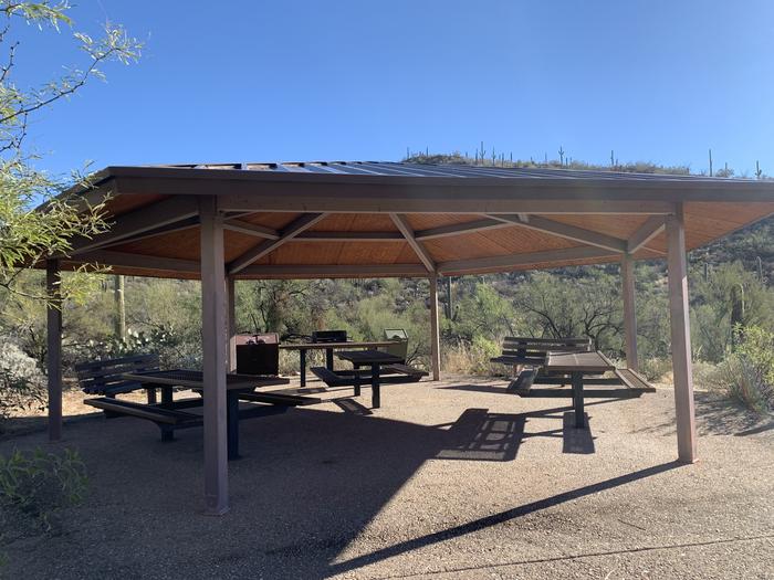 Cactus Ramada 2 includes 3 picnic tables and two benches, a grill and nearby trash and recycling receptacles underneath the structure.