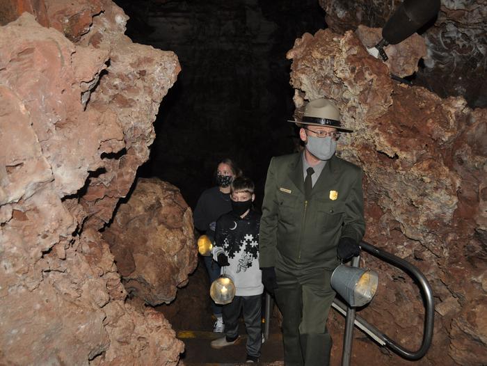 A park ranger and two children hold candle buckets while walking through a dark cave.Candlelight Tour participants must be 8 years and older and carry a candle bucket for light.