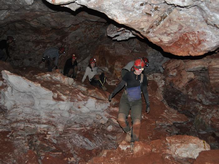 Cavers wear helmets and kneepads while crawling down a steep cave slope.The Wild Cave Tour includes substantial climbing and crawling in an off-trail environment.