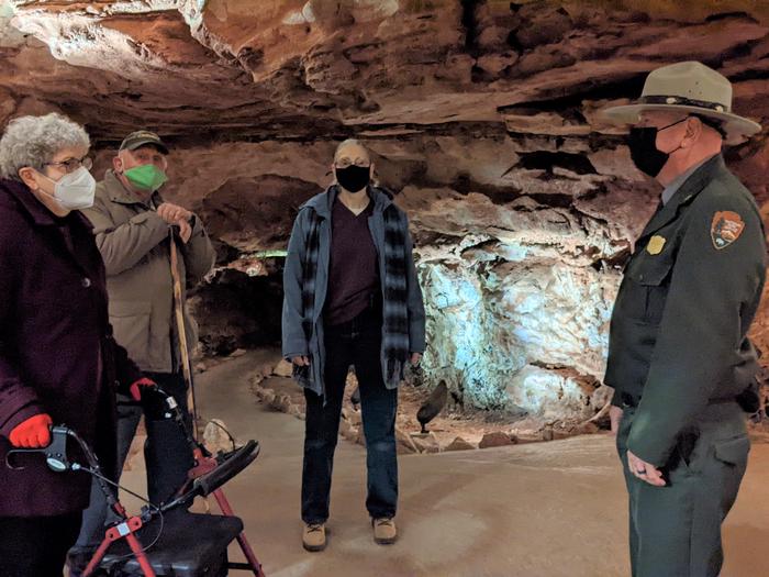 A ranger and three visitors, one with a walker, stand in a room of a cave.The 30-minute Accessibility Tour encounters no stairs.