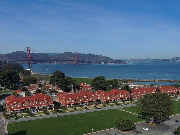 Red brick barrack buildings with lawn in front and the Golden Gate Bridge in the background.The historic Montgomery Street barracks are at the heart of the Presidio's Main Post area.