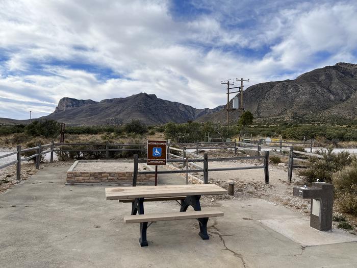 The site has two tent pads, one is raised for accessibility, both are surrounded by a wooden fence.  An accessible picnic table and drinking fountain are adjacent to the tent pads.  The Guadalupe Mountains are in the background.Frijole Horse Corral Campground has two tent pads a drinking fountain and picnic table.  The Guadalupe Mountains are visible in the distance.