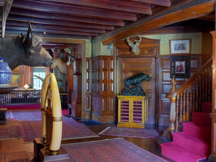 An interior hall with dark oak paneling, hunting trophies, and bronze sculptures.