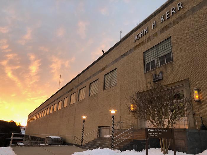 This is a picture of the John H Kerr Dam Powerhouse with the sun rising above it. There is snow on the ground. Welcome to John H Kerr Dam and Reservoir. This is the powerhouse located on the project. 
