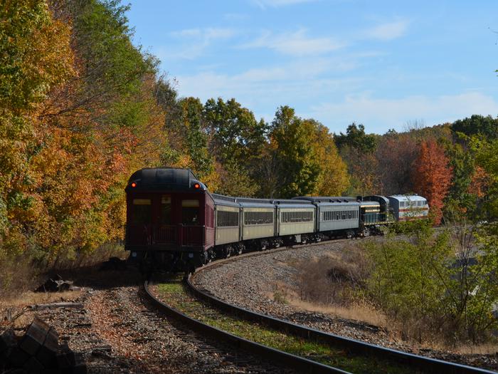 DL&W No. 663 pulling 6 cars and locomotives away from a train station, fall foliage in backgroundExperience the beauty of fall foliage during our autumn excursion trips.
