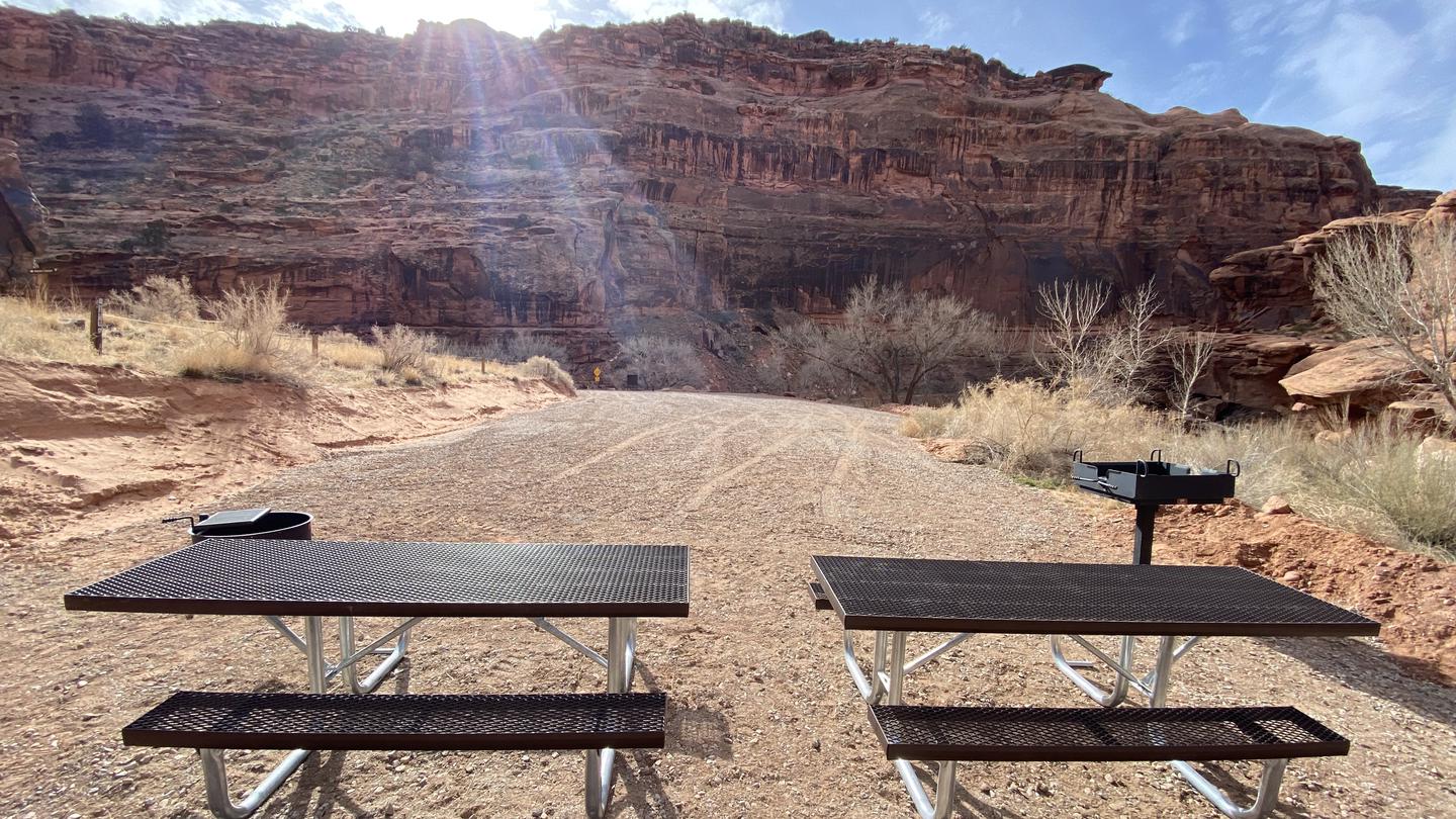 Group campsite, picnic tables, fire pit, and grill with sun setting behind cliffs in background