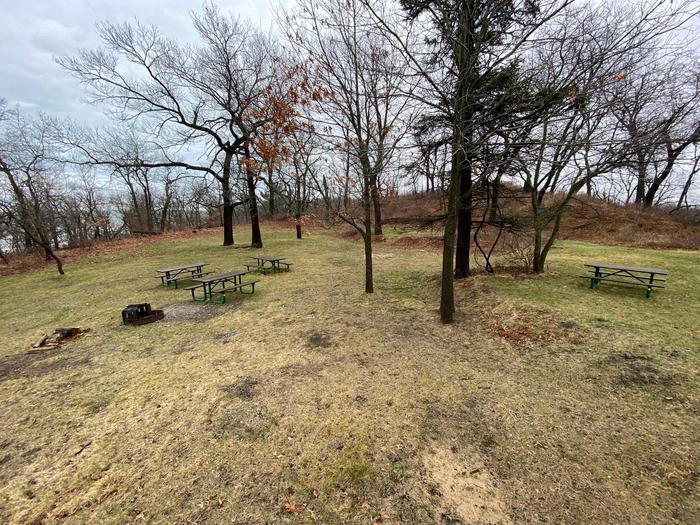 Picnic Tables and trees surround the open spaces of the Dunbar Group camp site.Picnic tables and a fire pit are available for use at the Dunbar group camp site.