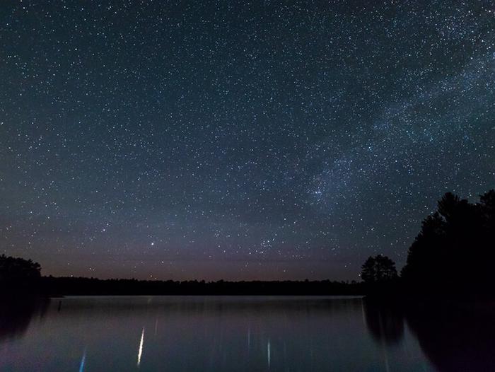 The Milky Way Galaxy stretches across the dark night sky over calm waters at Voyageurs