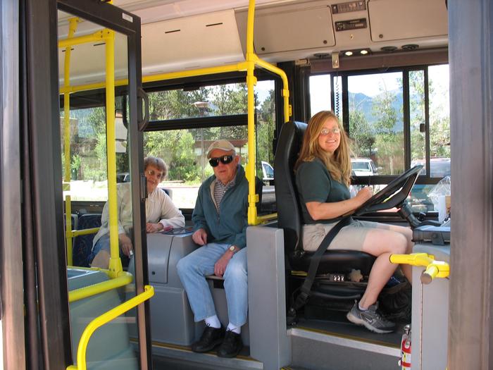 A view looking inside the bus. The bus driver and two passengers are looking towards the viewerA view looking inside the door of the Hiker Shuttle bus