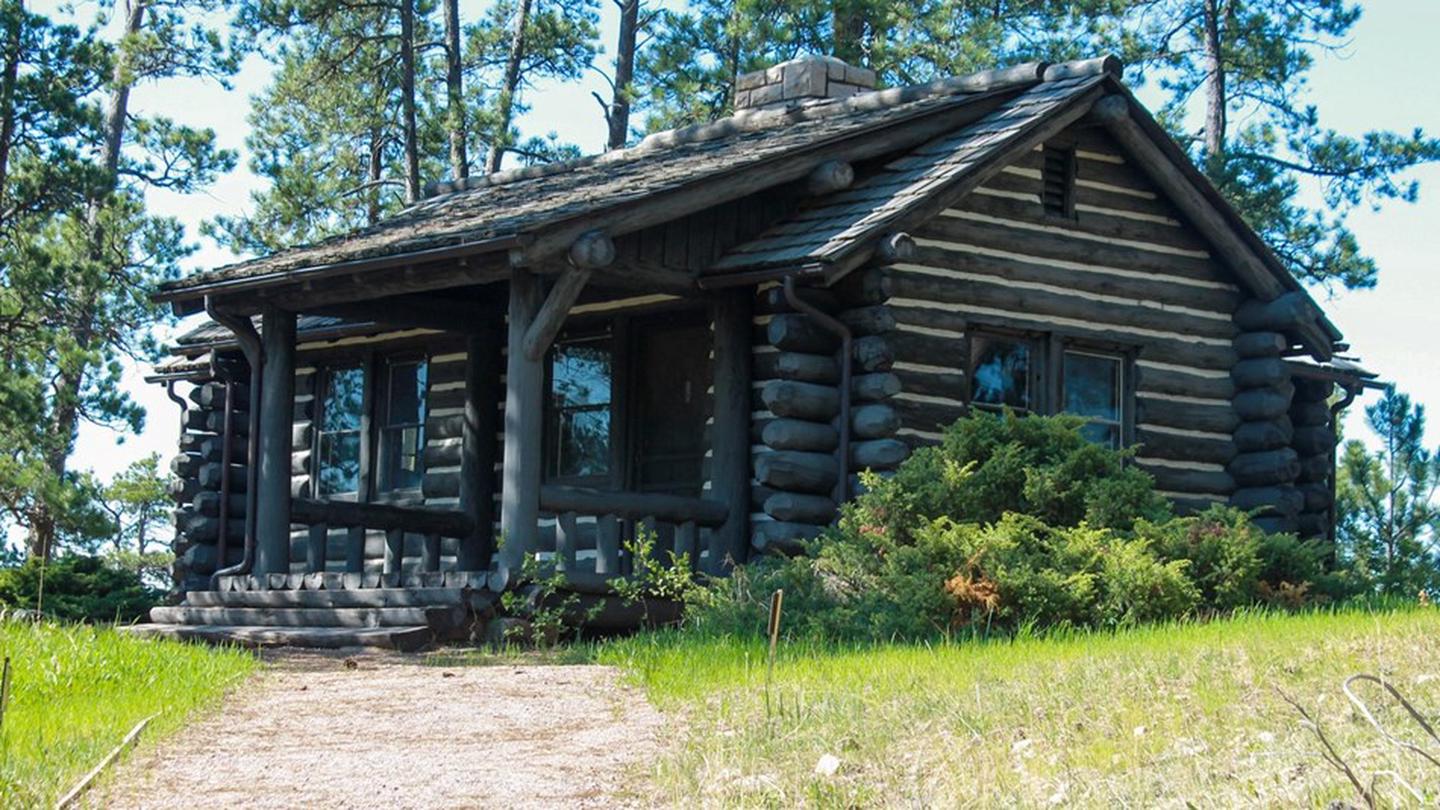 A rustic cabin surrounded by grass and trees.The Historic Lantern Tour meets in the Historic Area, home to a Civilian Conservation Corps-built cabin that served as the parks first visitor center.
