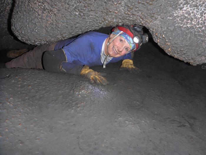 A person in caving gear crawls through a tight cave passage.The Wild Caving Tour has no shortage of belly-crawls and tight spaces.