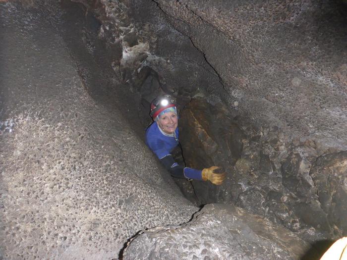 A person in caving gear looks up through a narrow cave passage.The Wild Caving Tour has several spots where scrambling and chimneying are required.