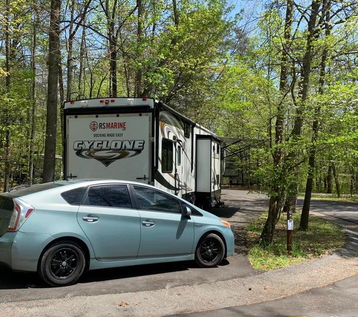 A light blue car with a white and black fifth-wheel on a blacktop surface.