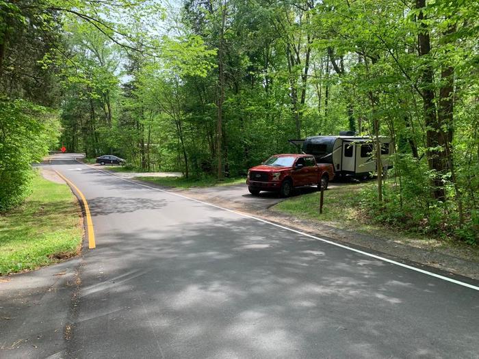 A red truck with a black and white trailer surrounded with green trees.B-1 site has nice space.