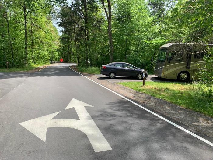 A blacktop surface with white arrows to direct the traffic, along with a navy car and brown RV.