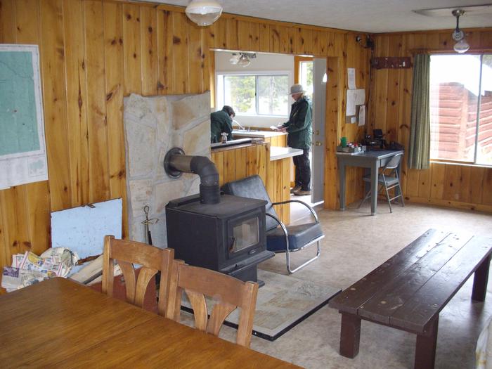 Living space with wood burning stove, dining table, and coffee table. Kitchen in background.Burgdorf Cabin - living space