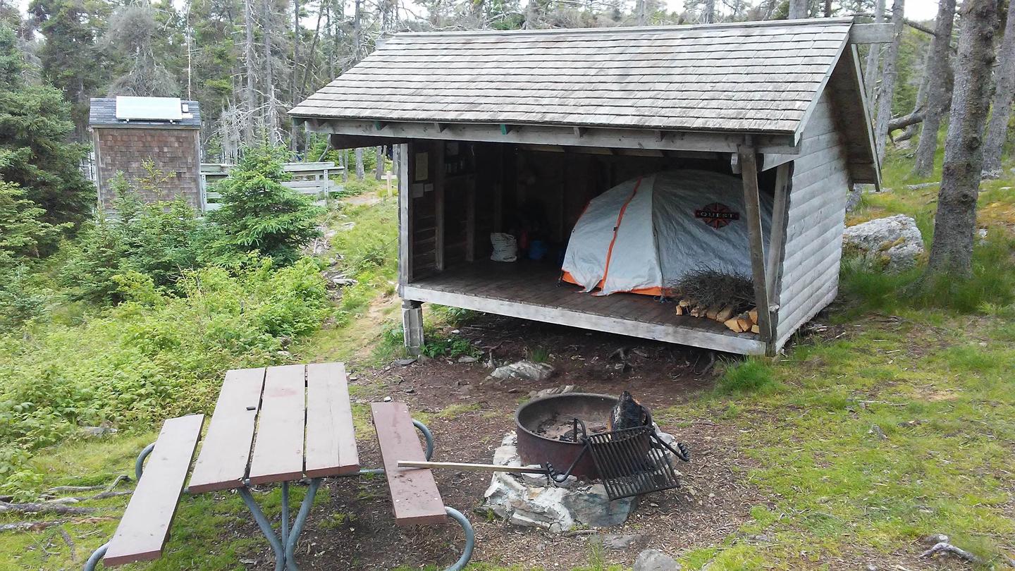 Tent shelter, fire ring and picnic table on grassy hillside.Site 3 at Duck Harbor Campground
