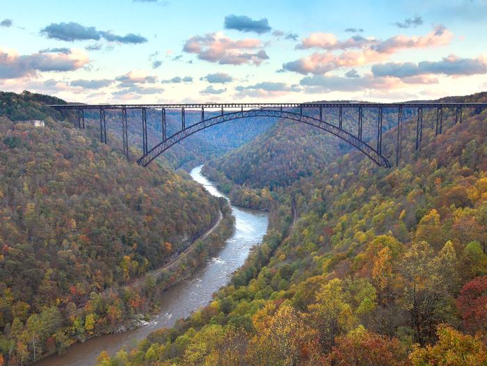 Color photo of a deep mountain gorge with a river running through the center with fall foliage covering the mountainside and a bridge spanning the gorge with a blue skyAfter a mile and a half walk through the forest the gorge revels itself on this moderate rated hike.