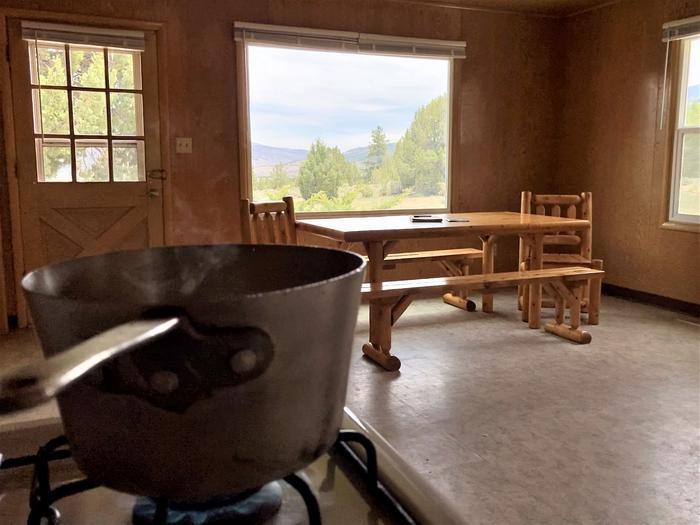 In the kitchen, a boiling pot sits on the gas stove in the foreground of Orange Olsen Dwelling dining area.A boiling pot sits on the gas stove in the kitchen of Orange Olsen Dwelling.