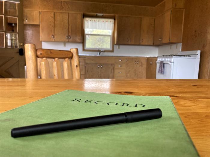 The community records notebook.A community records book where occupants write down their experiences and maintenance requests sits atop the dining table of Orange Olsen Dwelling.