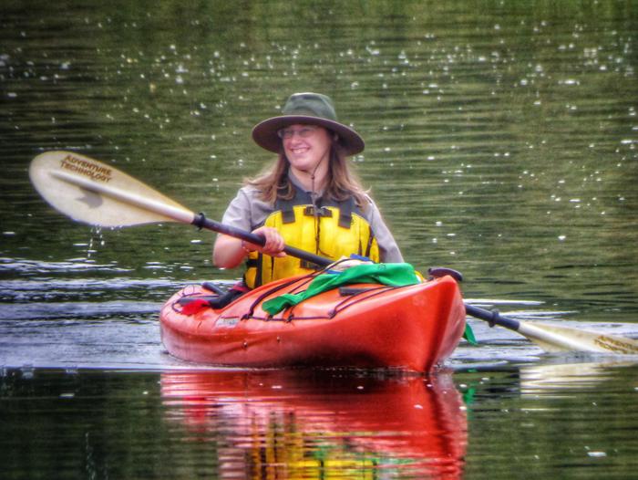 Park Ranger paddling a kayak on smooth green water.Ranger Esther leading a kayak program