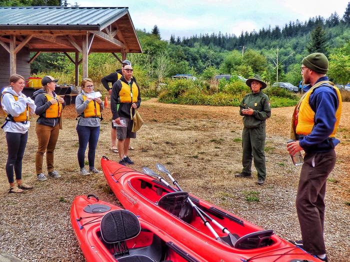 Six people in life jackets on land getting instructions from a ranger.Orientation to kayak tour