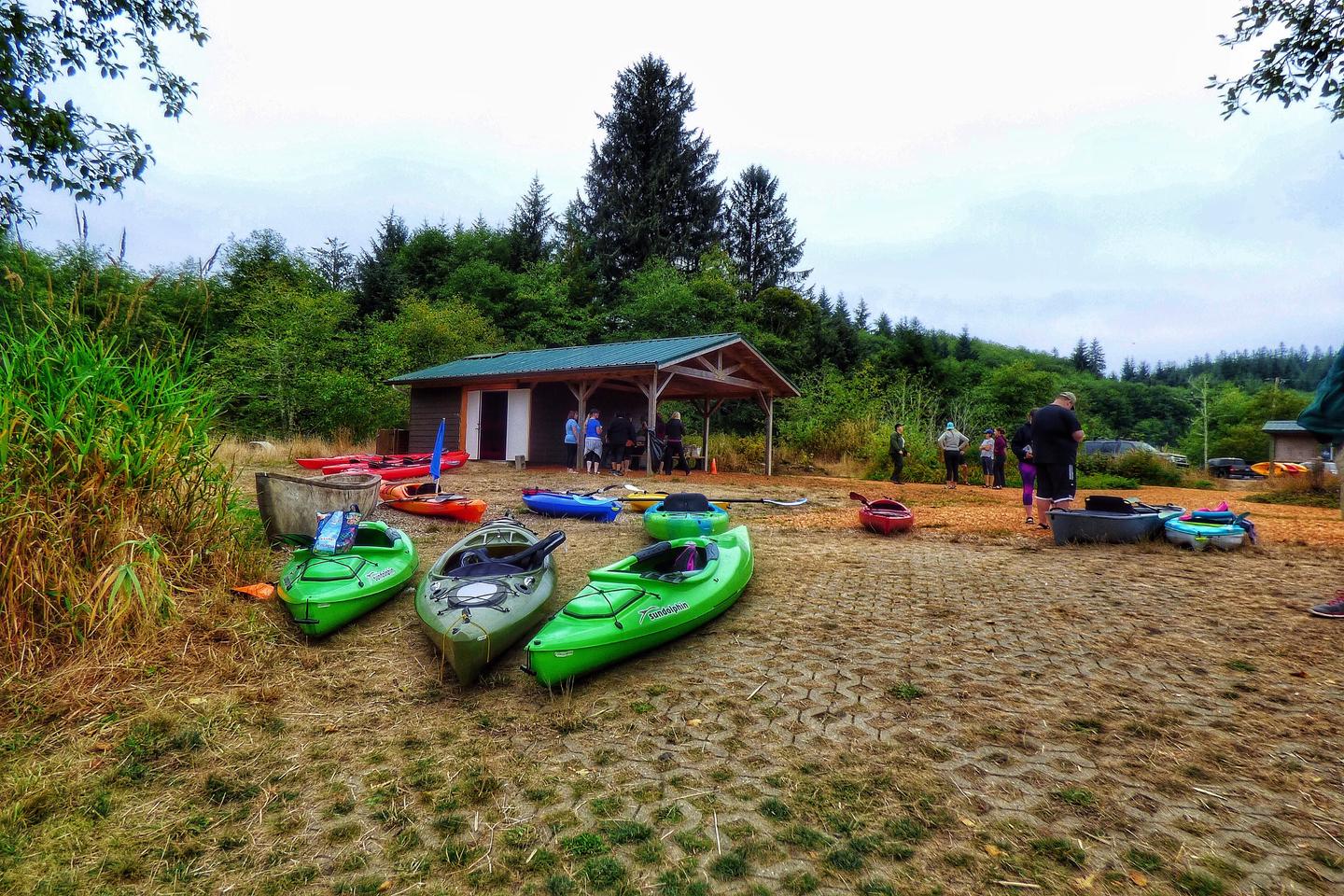 Assorted kayaks on the ground waiting to launch. Picnic shelter and parking lot in the background.Netul Landing kayak launch