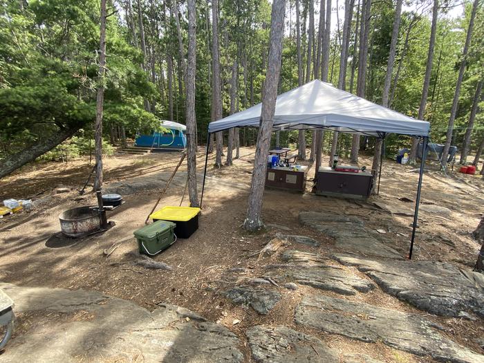 R19 - Logging Camp, view of campsite with camping gear all set up around the bear boxes and fire ring with a tent set up on the pad.View of campsite with gear