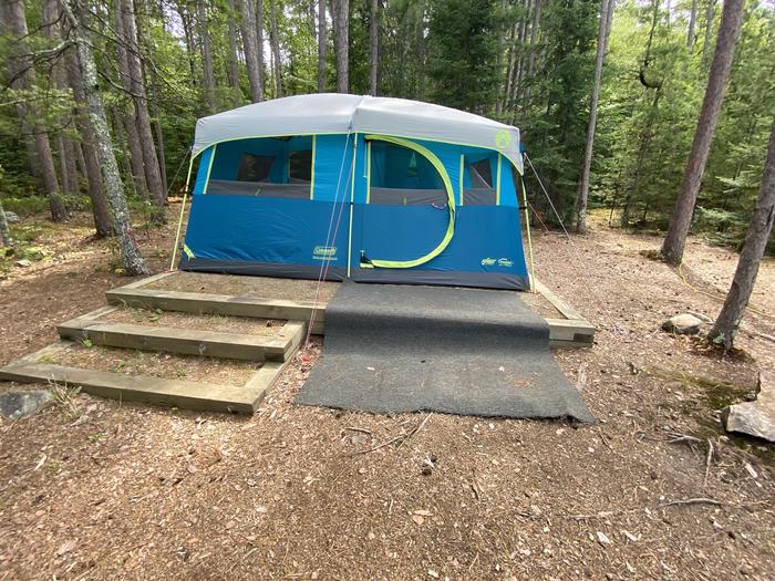R19 - Logging Camp, tent pad with a blue and green tent on it with stair on half of the tent pad.Tent pad with tent set up