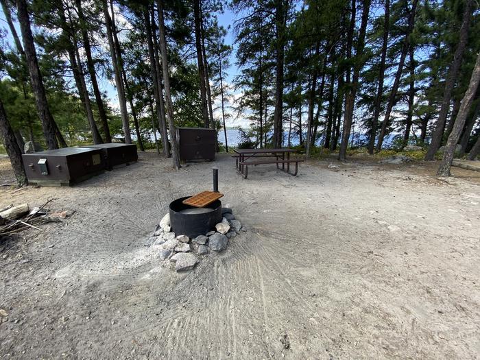 R27 - Virgin Island South, view looking into campsite with the fire ring surrounded by bear boxes and picnic tables.R27 - Virgin Island South campsite on Rainy Lake
