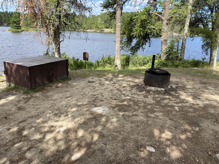 R71 - Loon Cove, view looking out from campsite of the bear box and fire ring with the water in the background.R71 - Loon Cove campsite on Rainy Lake
