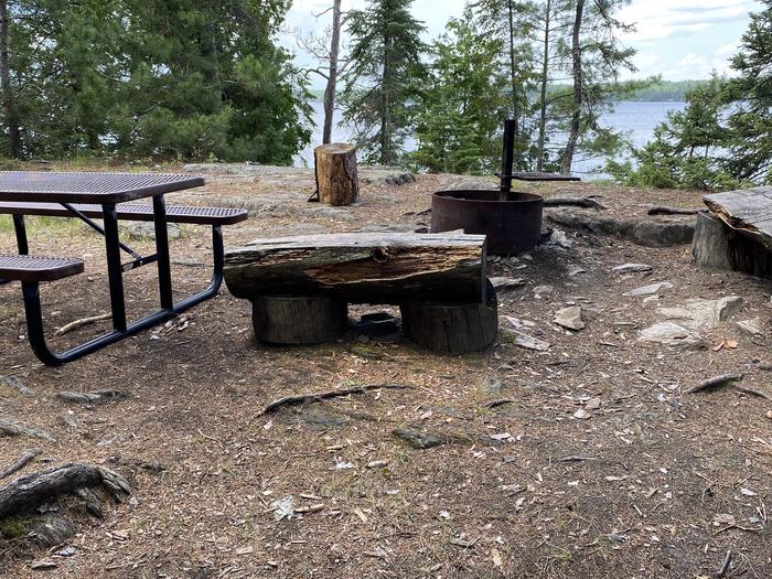 R72 - Rock Shelf, view looking out from campsite view wood benches and picnic tables surrounding a fire ring.R72 - Rock Shelf campsite on Rainy Lake